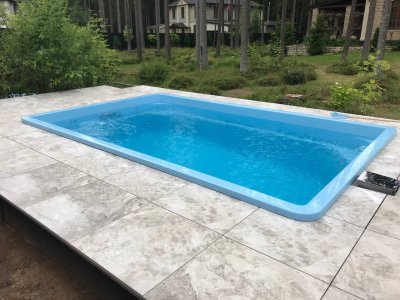 Прямоугольный голубой бассейн с мраморной серой плиткой на улице